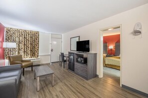 Une chambre d’hôtel équipée d’une télévision, d’un bureau, d’une chaise, d’un lit et d’une salle de bain visible à travers une porte ouverte.