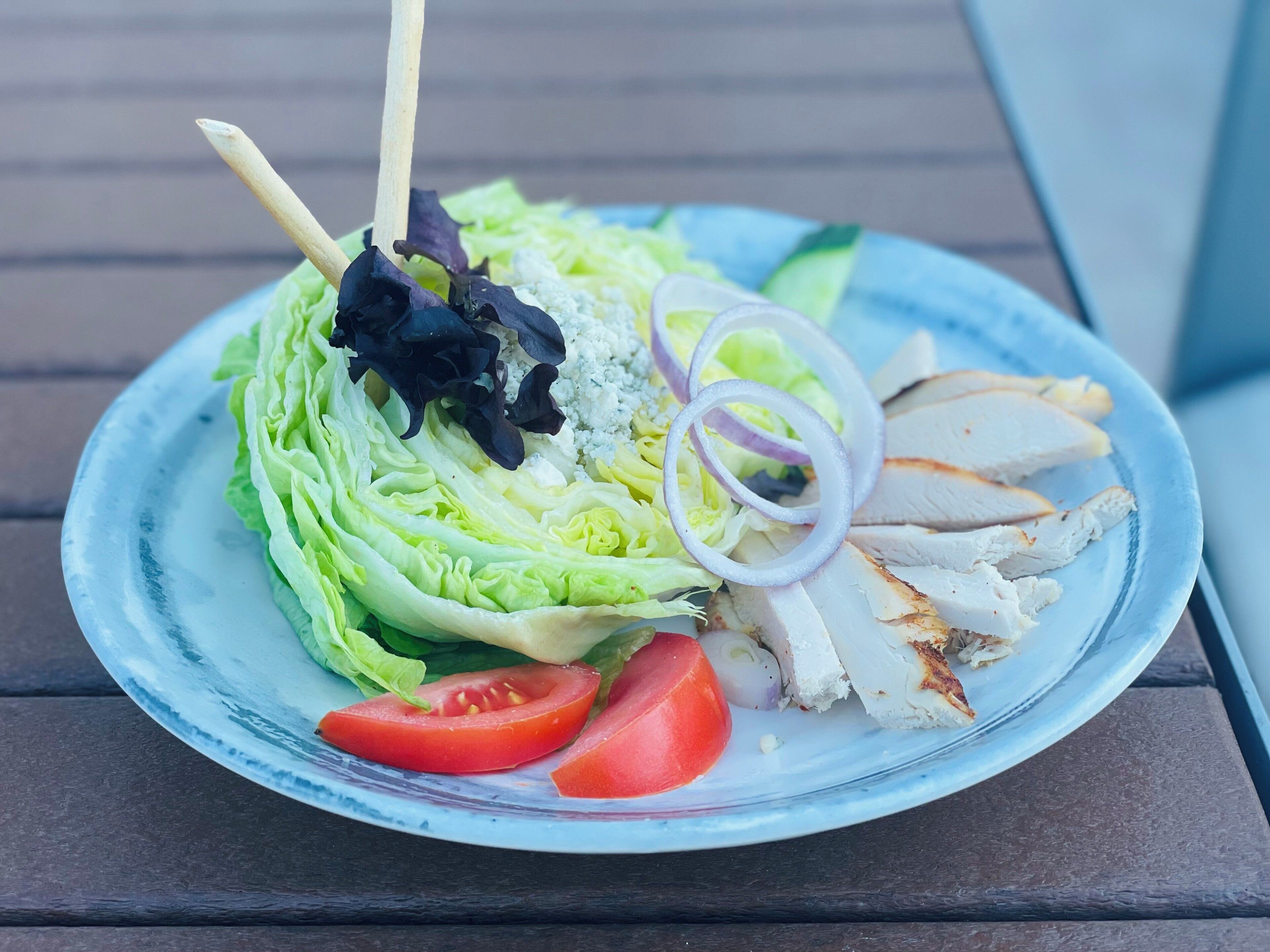 A plate with grilled chicken, lettuce, red onion, and tomato slices.