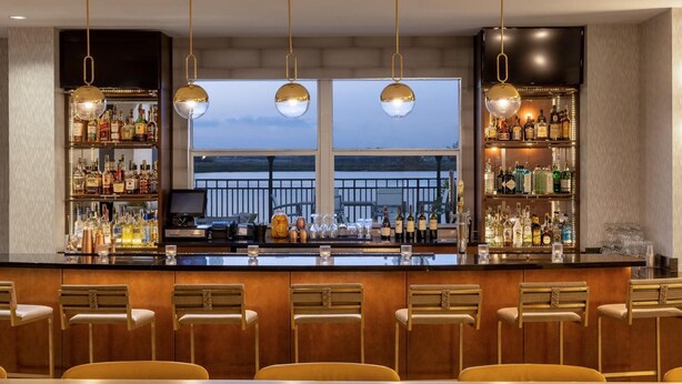 A bar area with a long counter, multiple shelves of liquor bottles, and several bar stools.