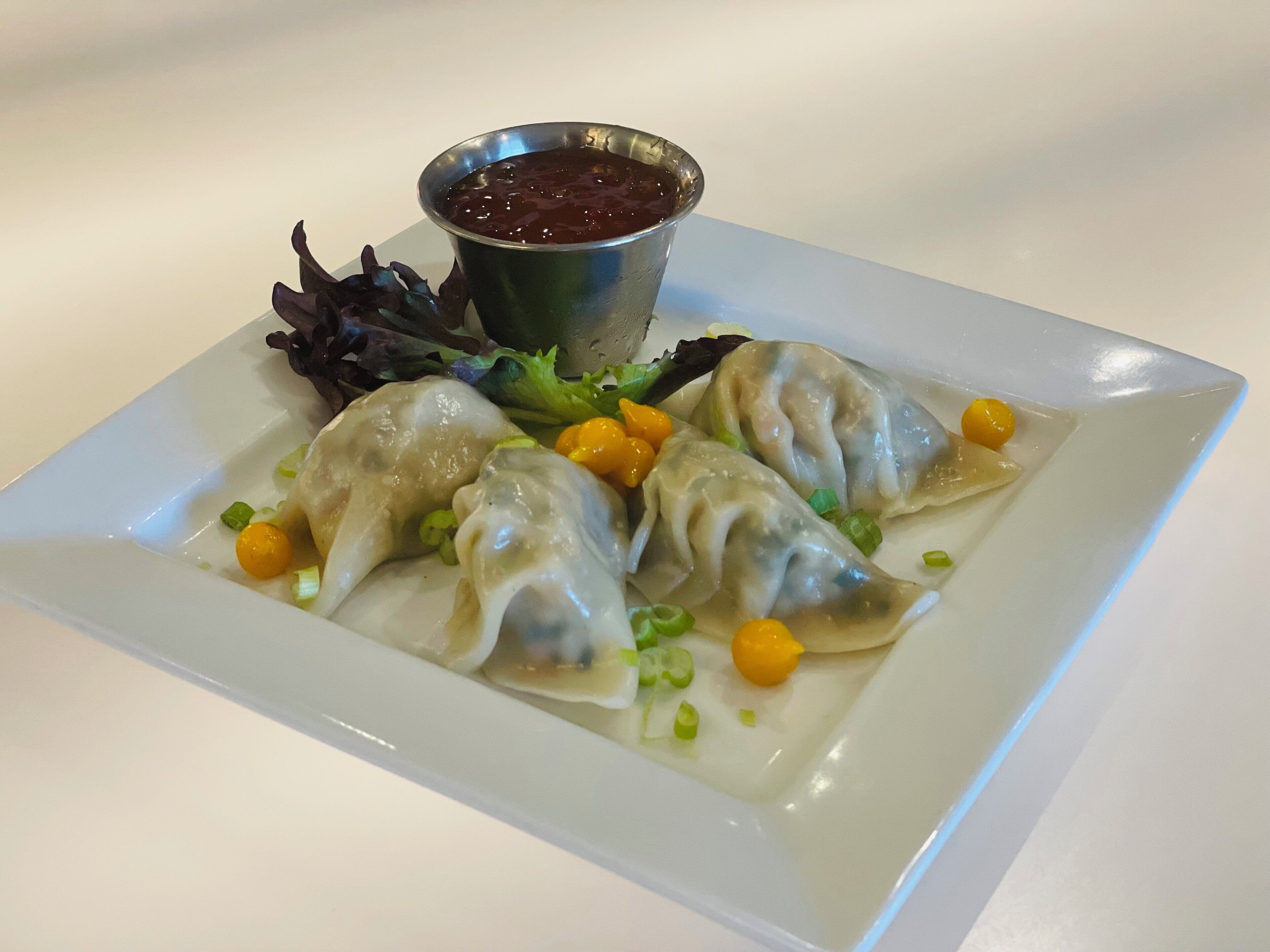 A plate of dumplings with a side of sauce and garnish.