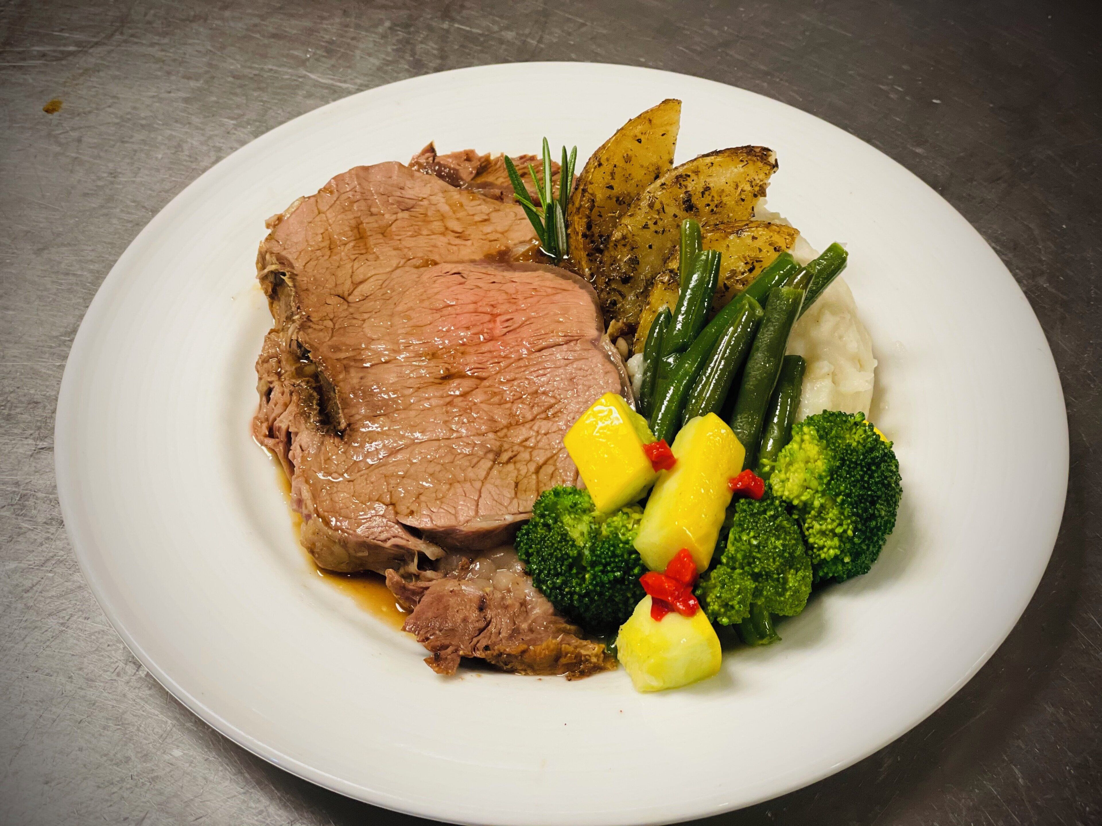 A plate of food with beef, potatoes, green beans, broccoli, and a garnish.