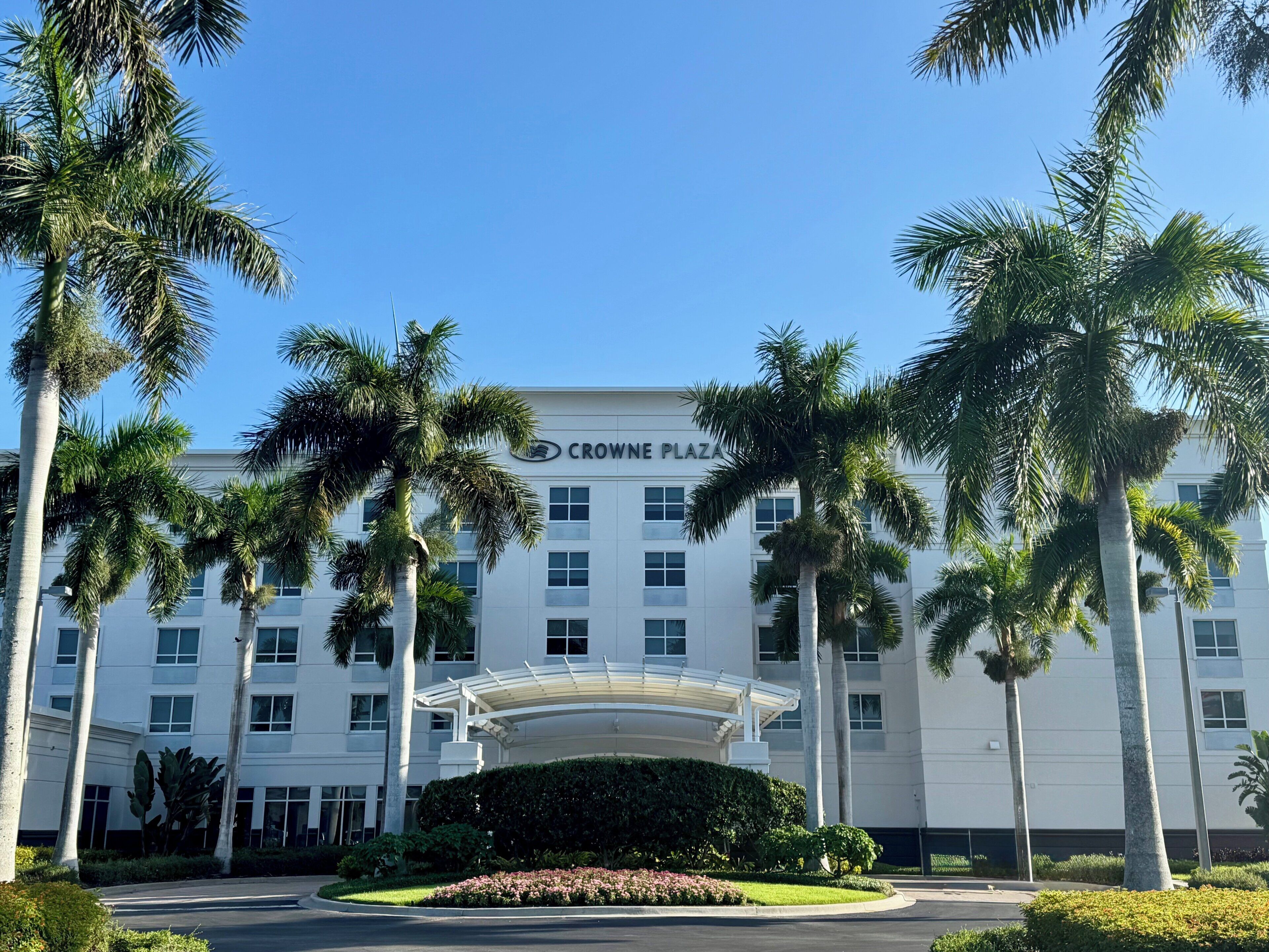 A hotel with a white facade, palm trees, and a covered entrance.