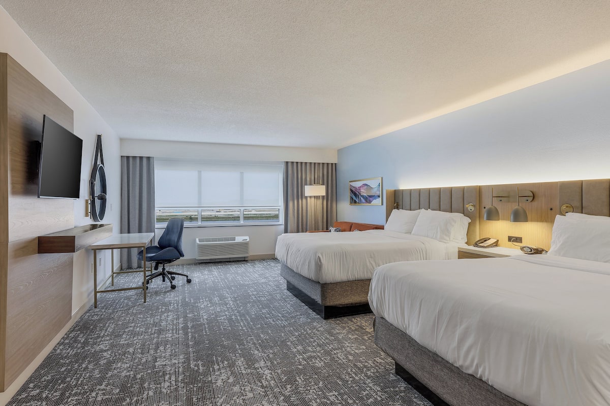 A hotel room with two beds, a desk, a chair, a TV, and a window with curtains.