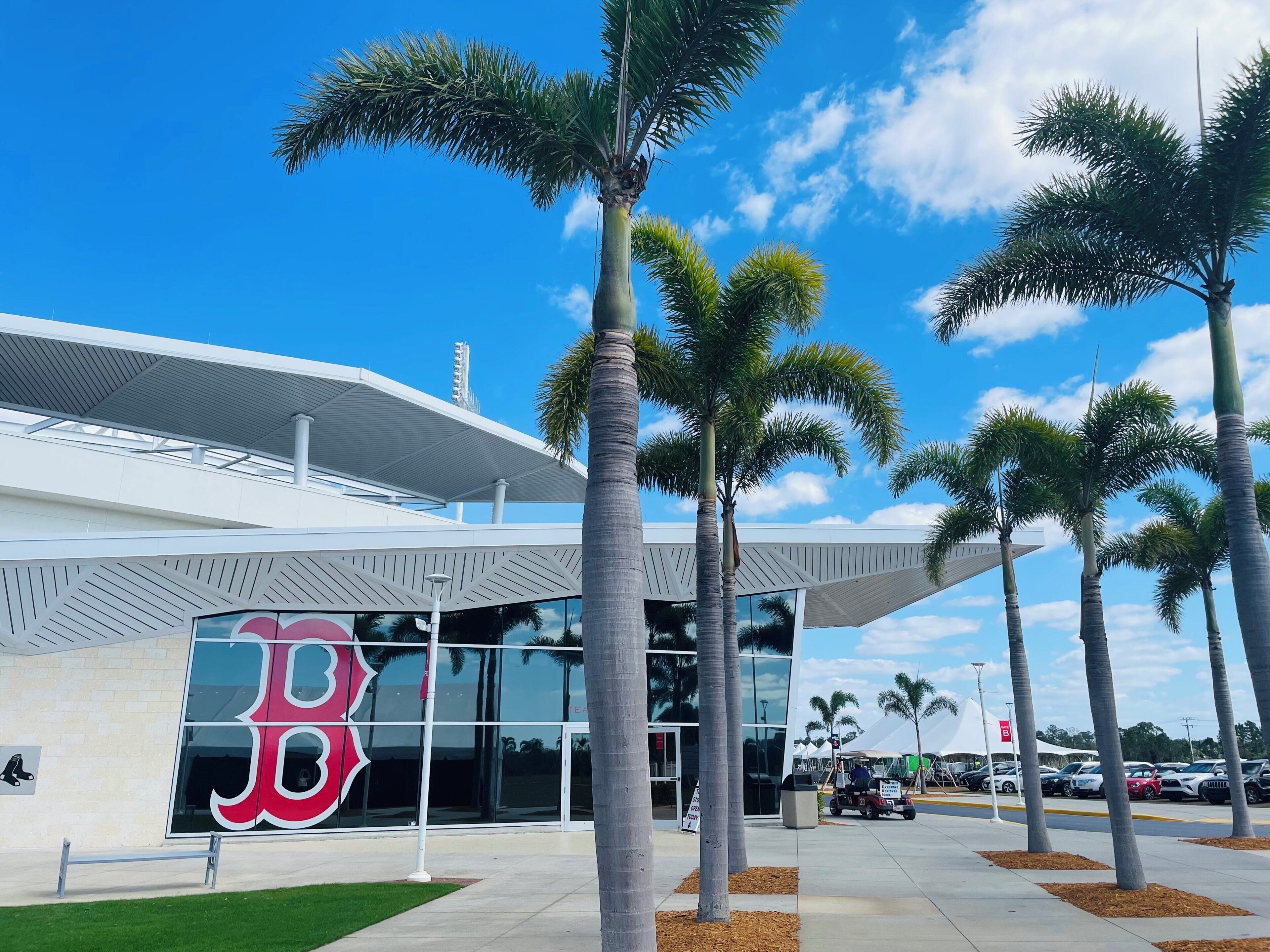 A modern building with a large glass facade, palm trees, and a clear blue sky.
