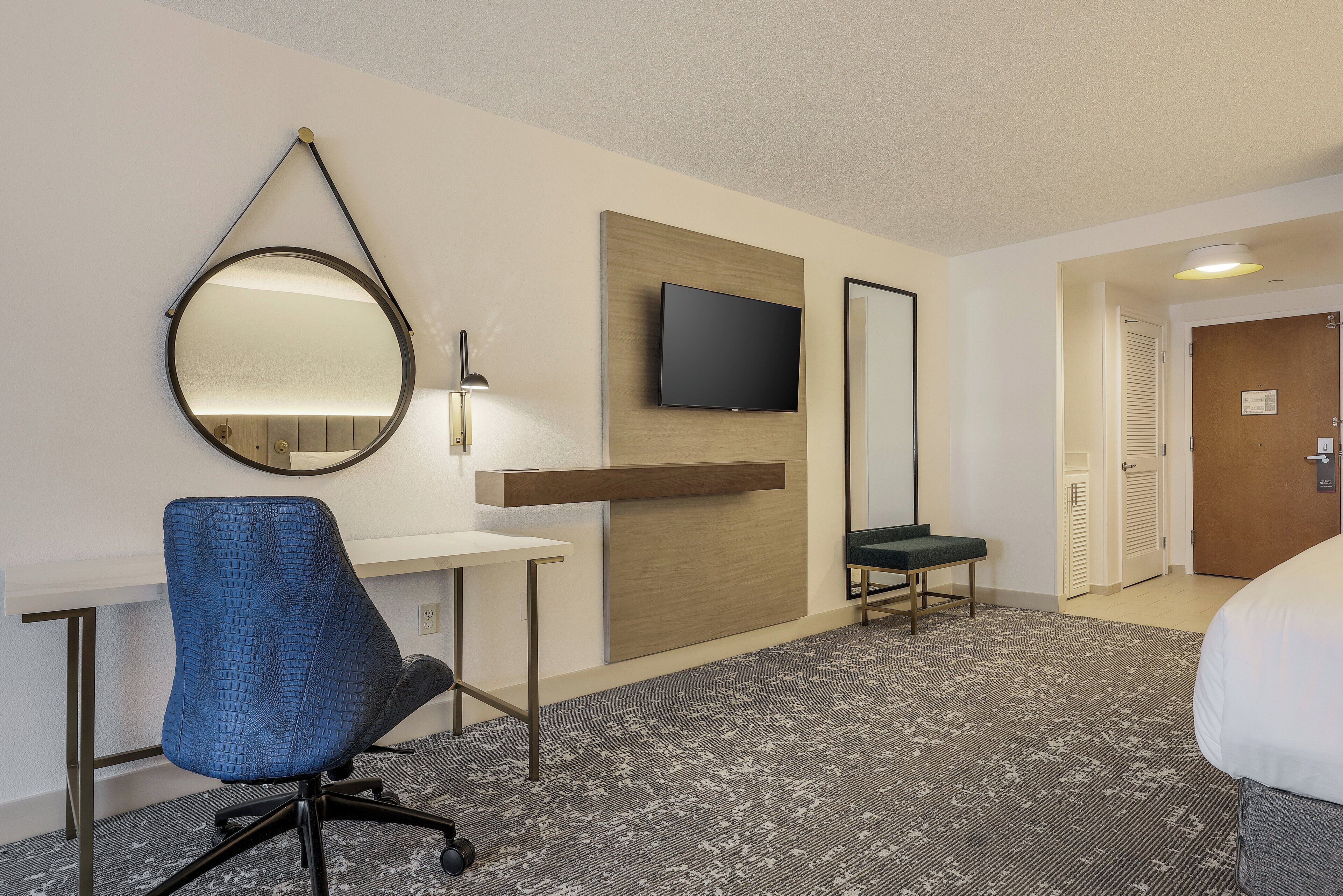 A hotel room with a desk, chair, television, and a bed.