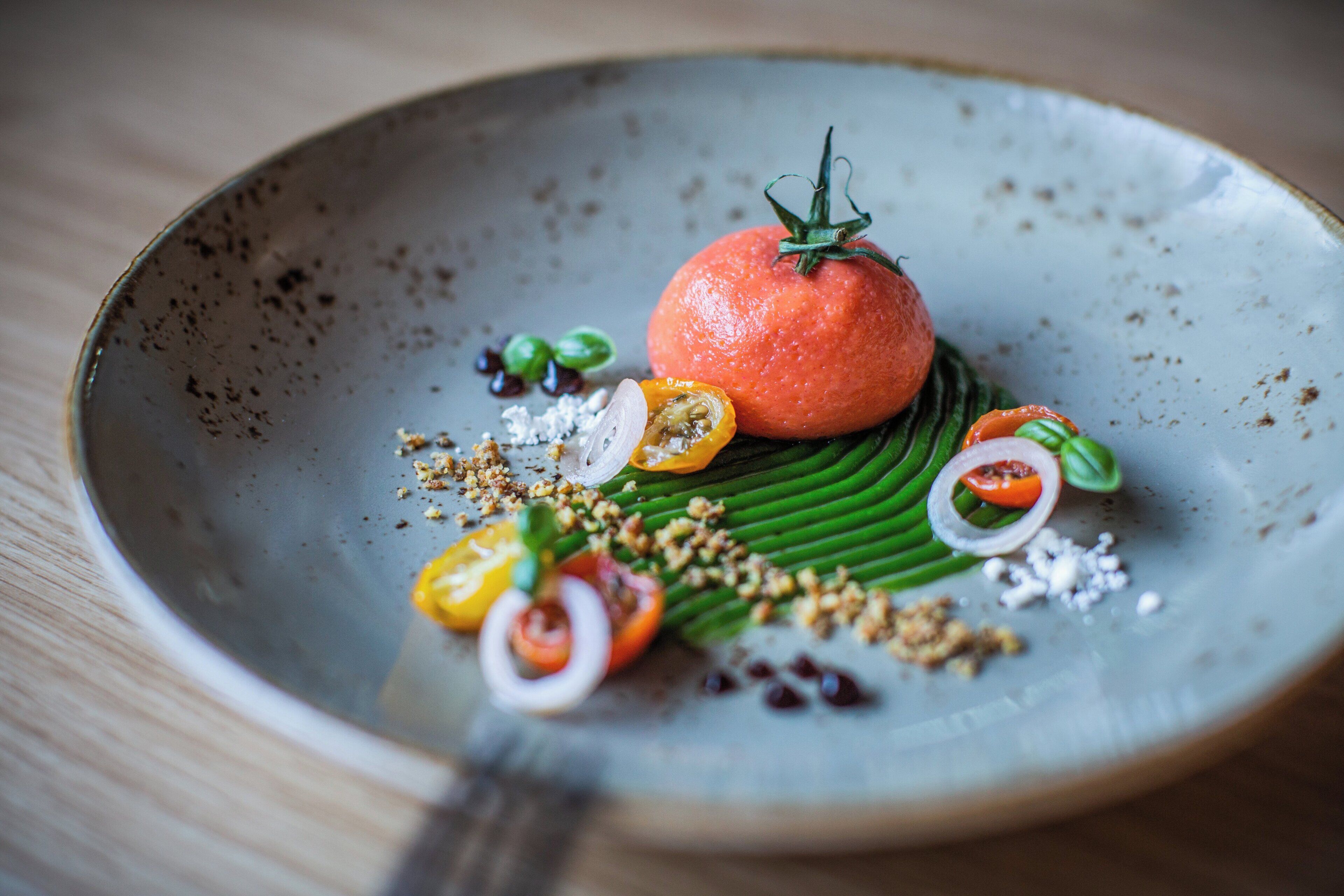 A plate with a tomato centerpiece, green leaves, and various garnishes.