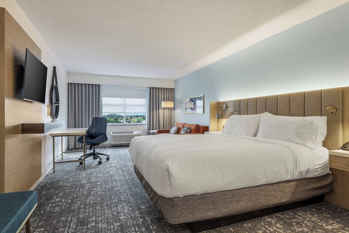 A hotel room with a bed, desk, chair, and a TV mounted on the wall.