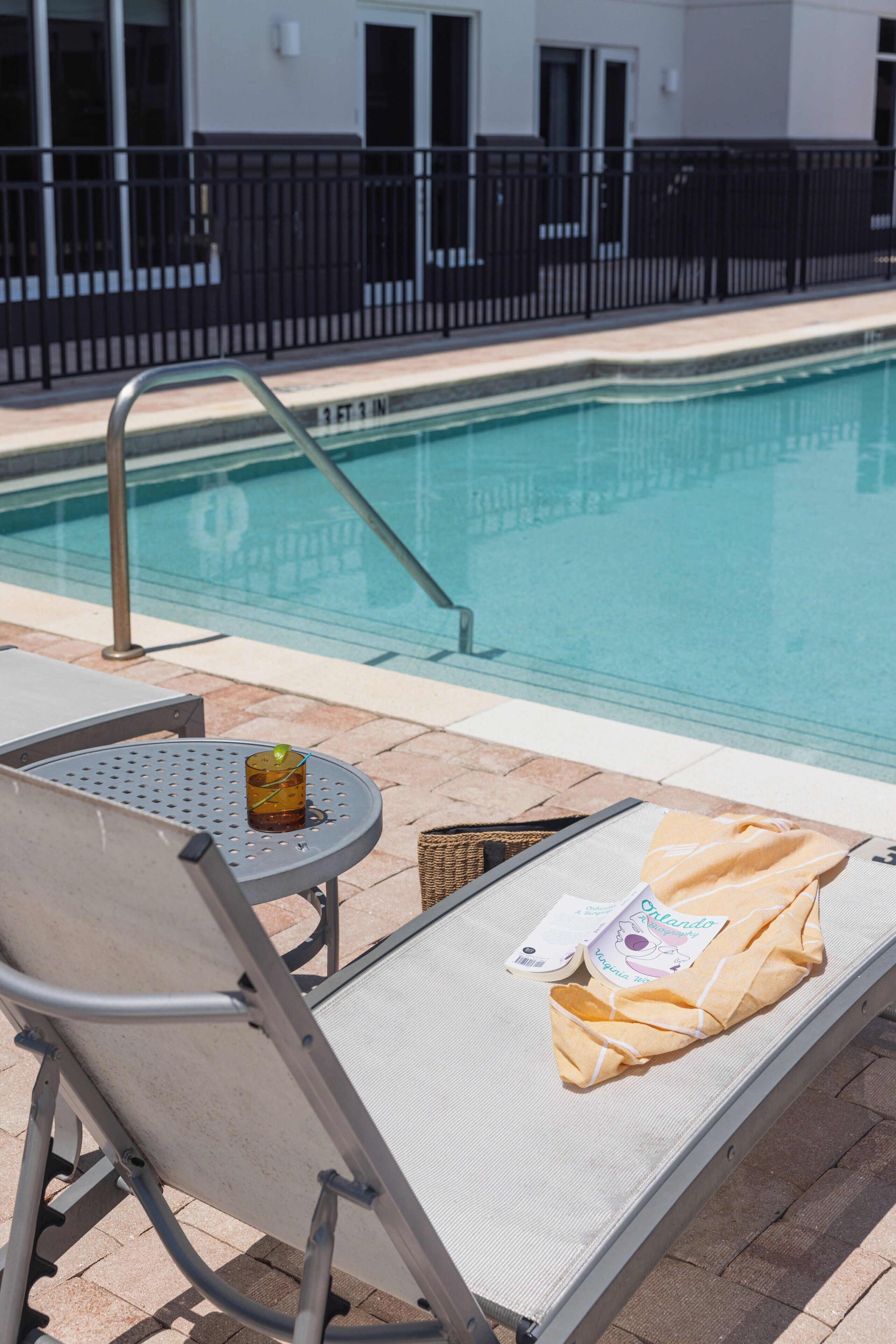 A poolside area with lounge chairs, a small table, and a pool.