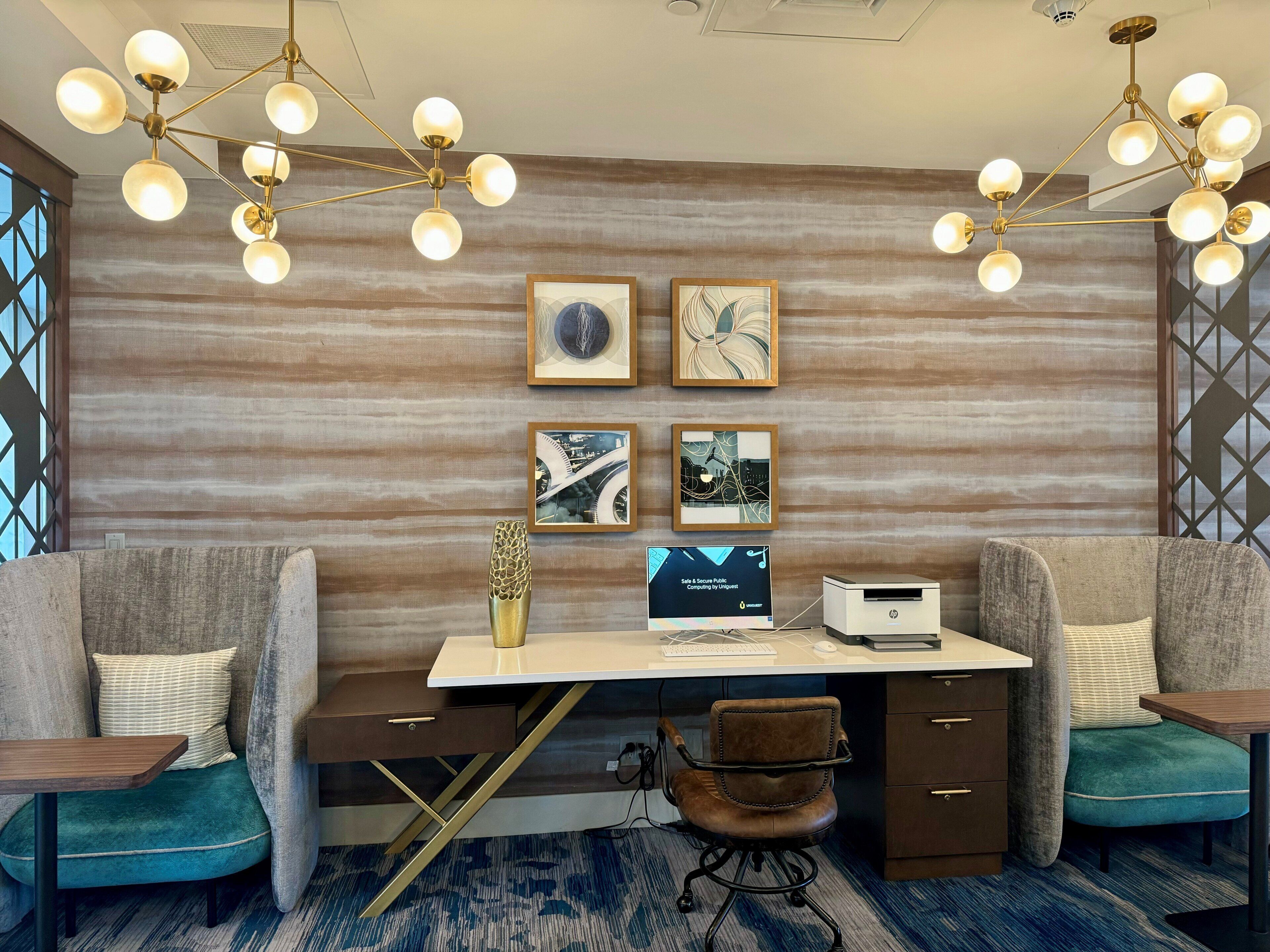 A modern office space with a desk, two chairs, a decorative ceiling light, and framed artwork on the wall.