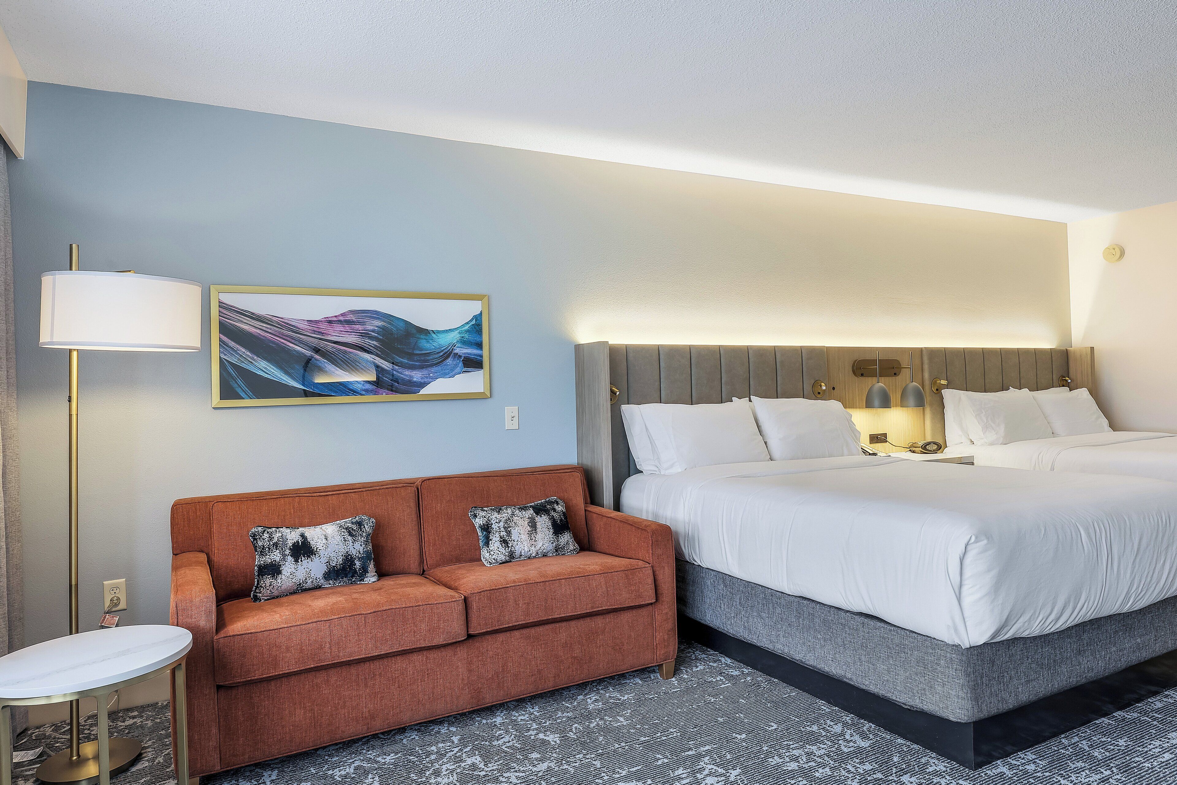 A hotel room with a bed, a sofa, a lamp, and a painting on the wall.