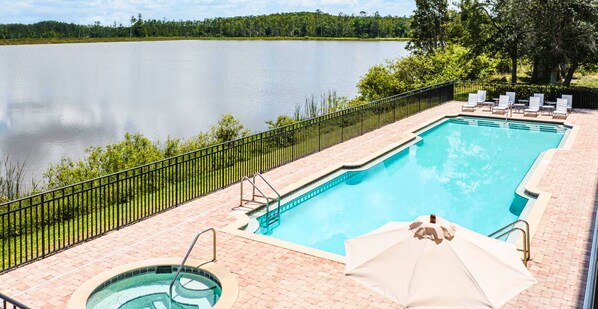 A rectangular swimming pool with a tiled deck, a hot tub, and lounge chairs with umbrellas.