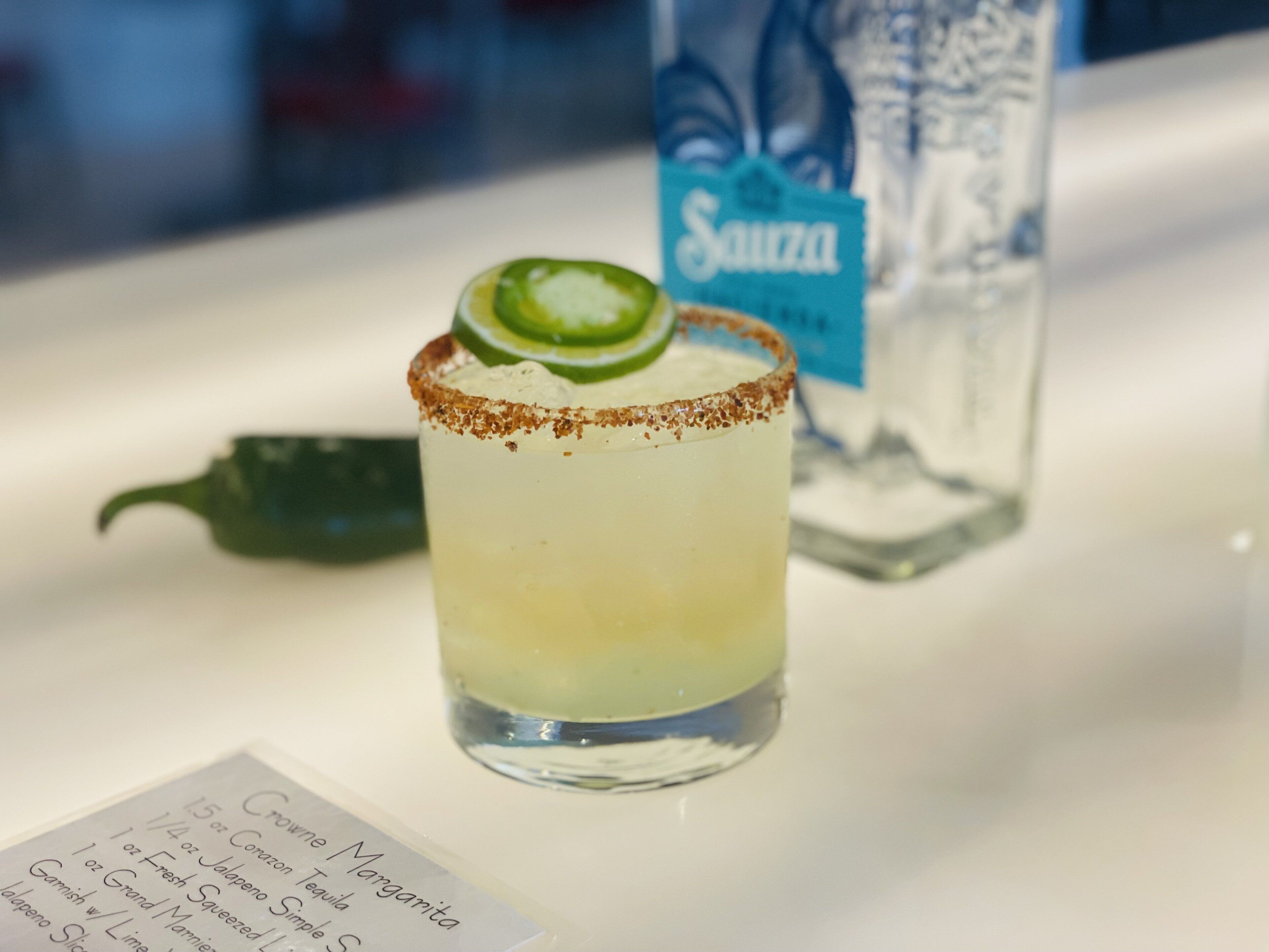 A cocktail with a salted rim, garnished with a slice of lime, and a menu with drink ingredients.