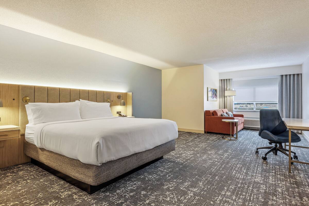 A hotel room with a large bed, a desk, a chair, and a sofa.