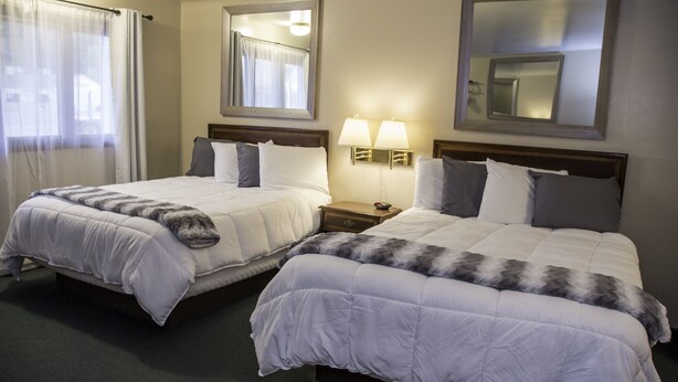 Une chambre d’hôtel avec deux lits, une table de chevet avec des lampes et un grand miroir au mur.