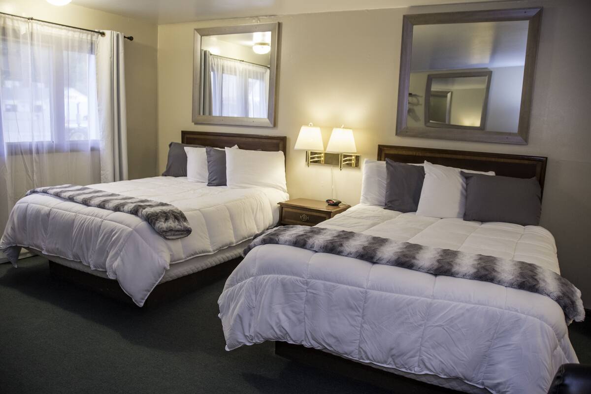 A hotel room with two beds, a nightstand with lamps, and a large mirror on the wall.