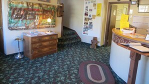 Une pièce avec un bureau en bois, un petit escalier, un mur orné d’un tableau d’affichage et un tapis à motifs.