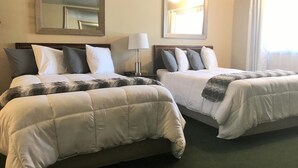 Deux lits queen-size avec des têtes de lit assorties, une table de chevet avec une lampe, un grand miroir au-dessus des lits et une fenêtre avec des rideaux.