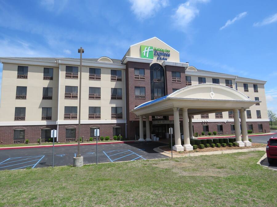 A Holiday Inn Express & Suites hotel with a covered entrance, parking lot, and a red car parked in front.