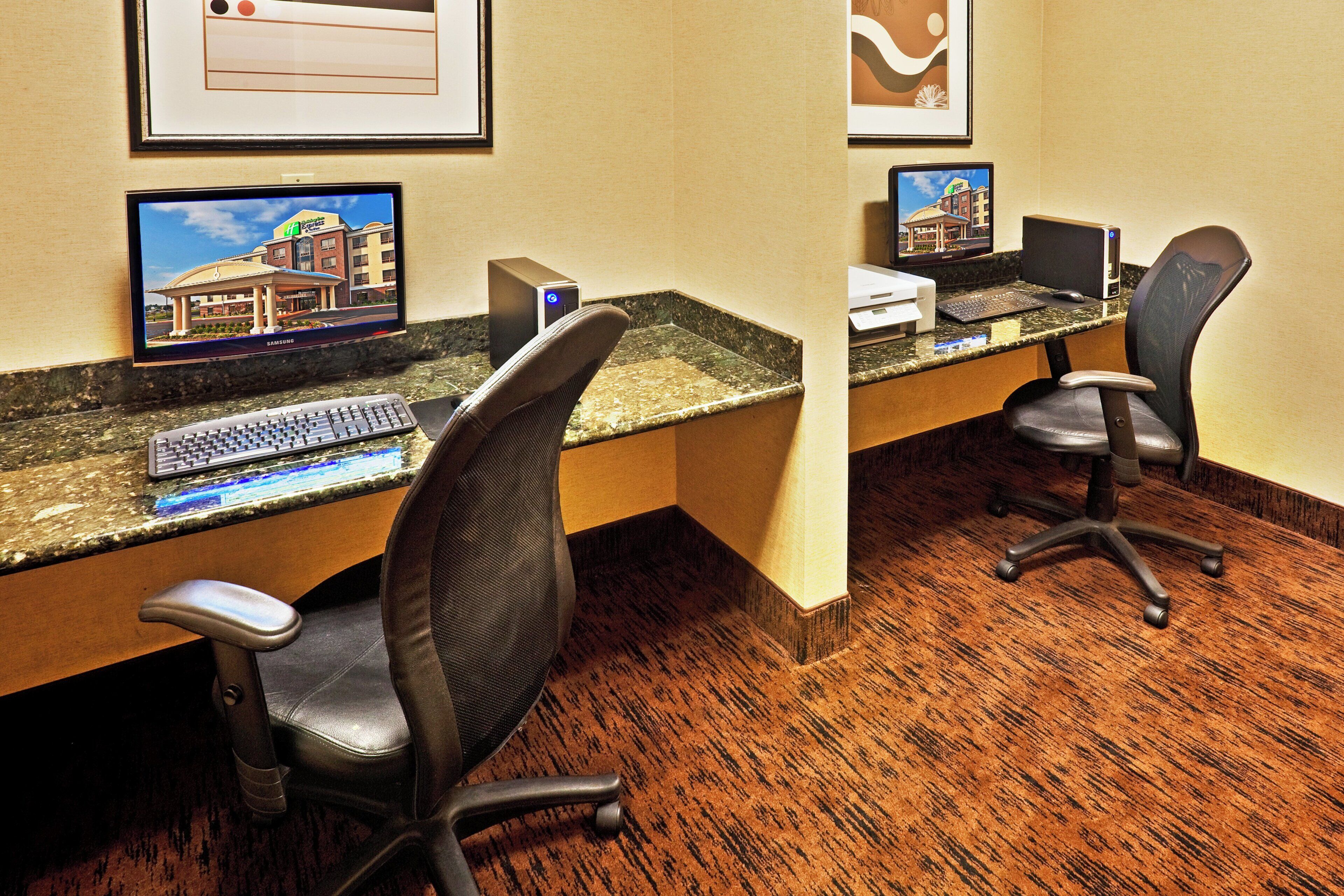 A hotel workspace with two desks, each equipped with a computer, keyboard, and chair.