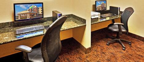 A hotel workspace with two desks, each equipped with a computer, keyboard, and chair.