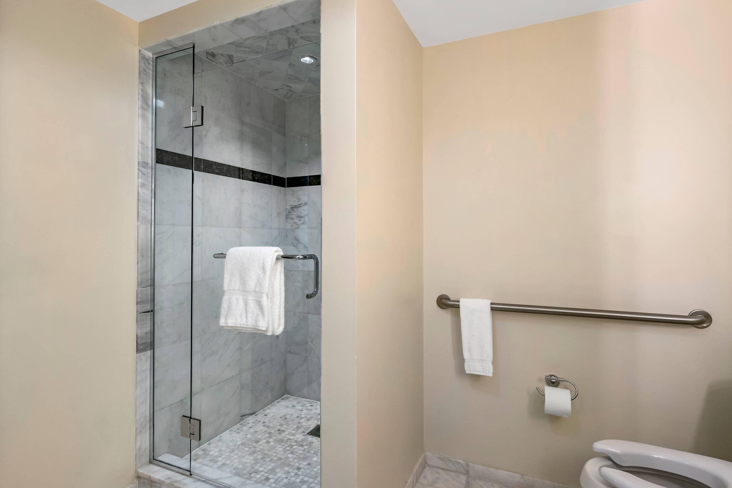 Un baño con ducha acristalada, inodoro con barra de apoyo y perchero.