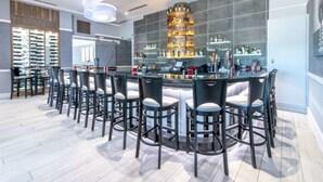 Zona de bar moderna con barra circular, varios taburetes y una gran variedad de botellas y vasos en estantes.