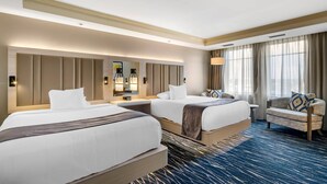 Habitación de hotel con dos camas, un sofá, un espejo grande y vistas al exterior.
