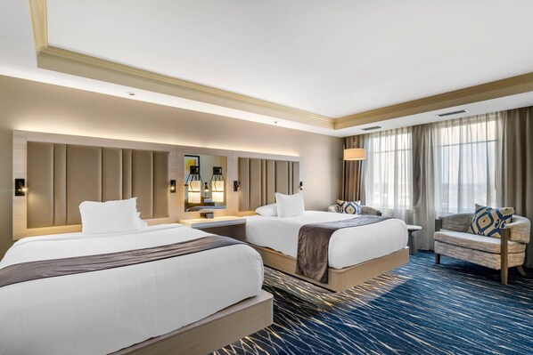 A hotel room with two beds, a sofa, a large mirror, and a view of the outdoors.