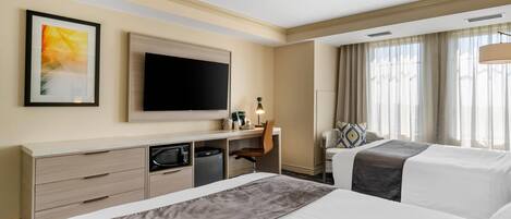A hotel room with two beds, a desk with a chair, a flat-screen TV, and a window with curtains.