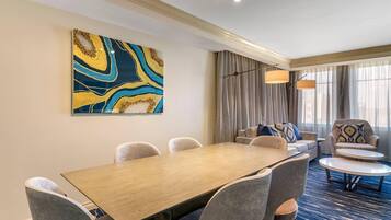 A hotel room with a dining area featuring a wooden table and chairs, a sofa, and a large abstract painting on the wall.