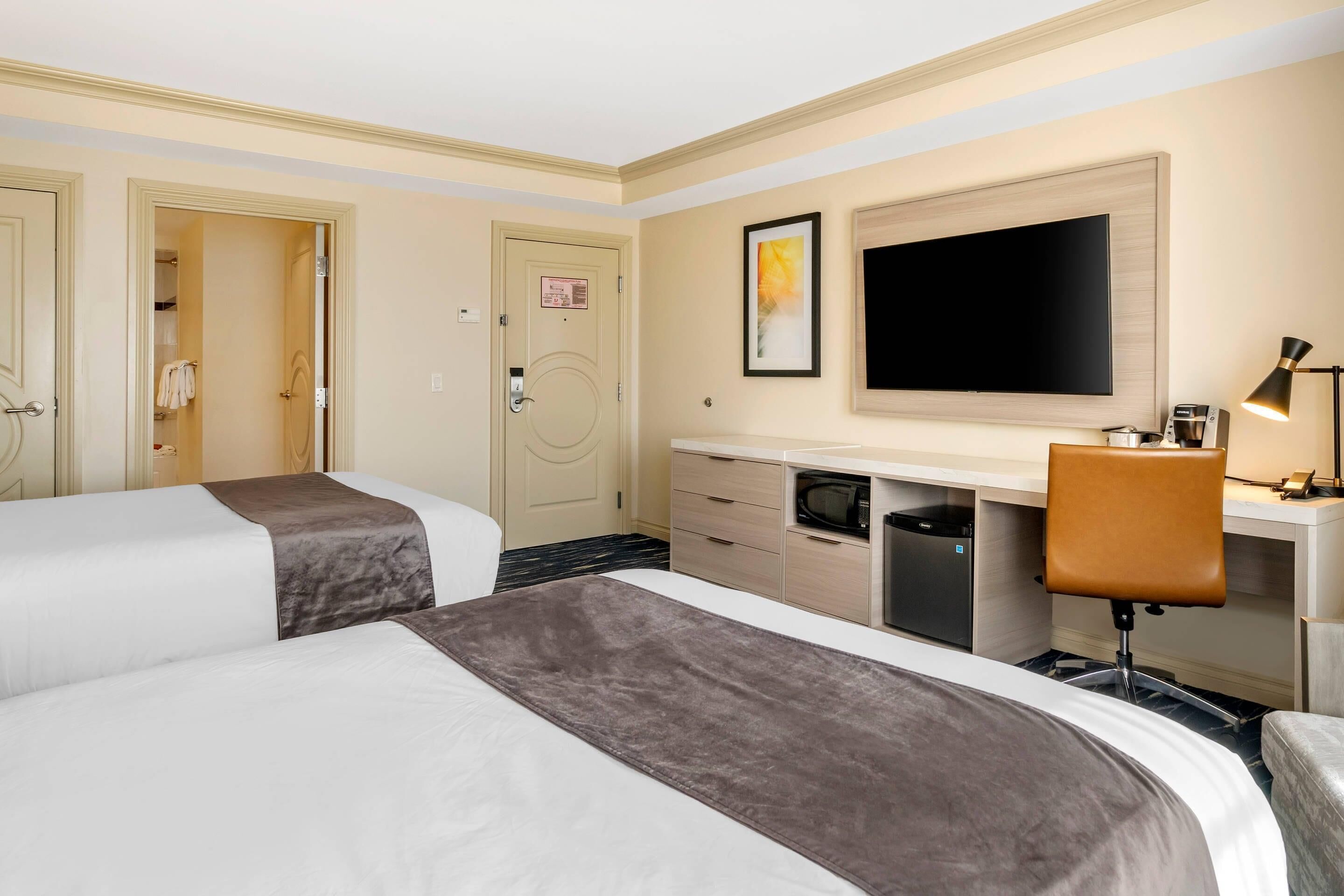 A hotel room with two beds, a desk, a chair, a television, and a microwave.