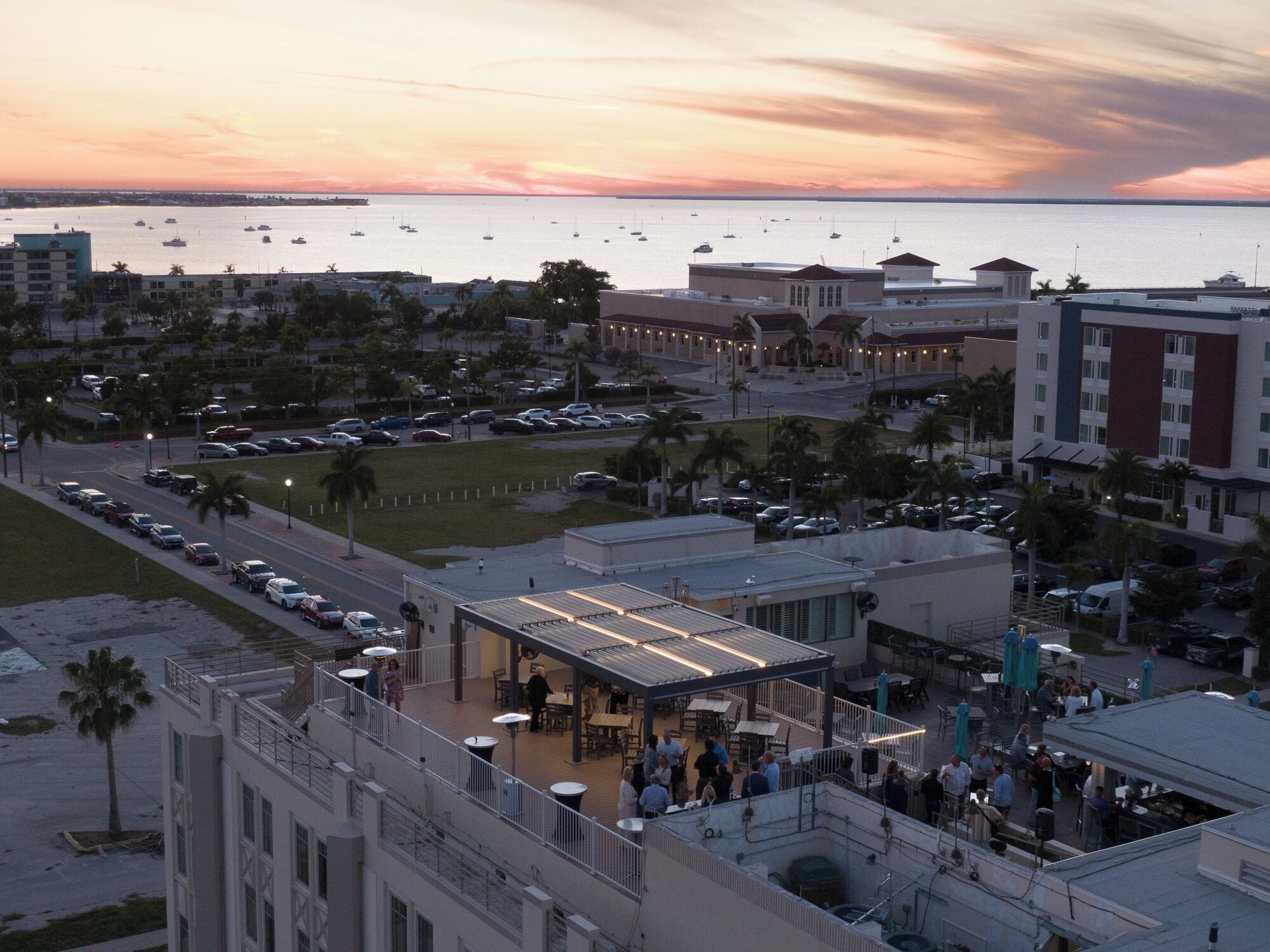 A rooftop bar with outdoor seating overlooking a marina and cityscape at sunset.
