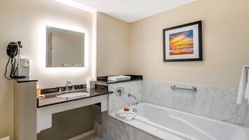 A modern bathroom with a large mirror, a sink, a bathtub, and a framed sunset painting on the wall.