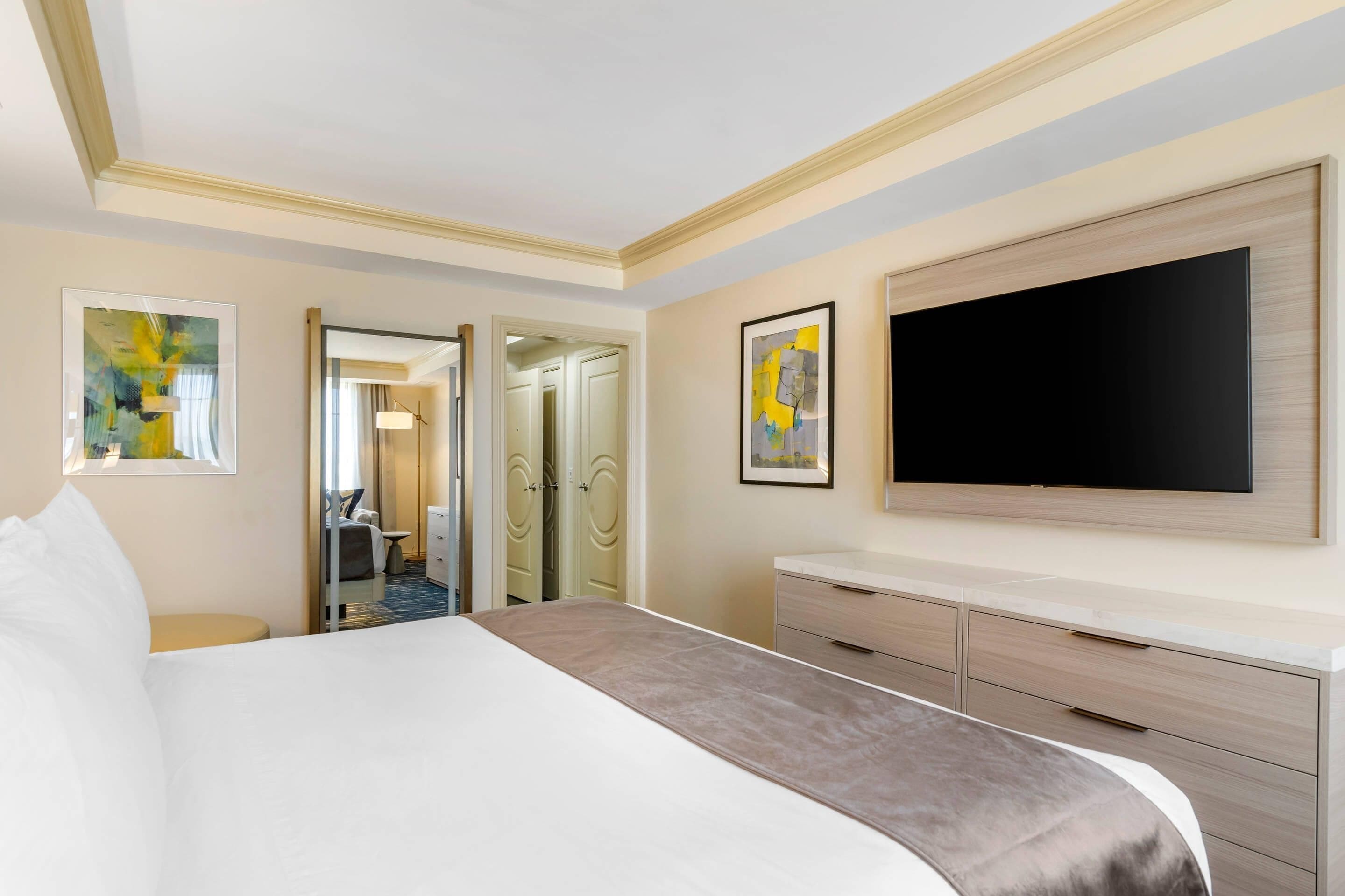 Habitación de hotel con una cama grande, un televisor de pantalla plana en la pared y un escritorio con cajones.