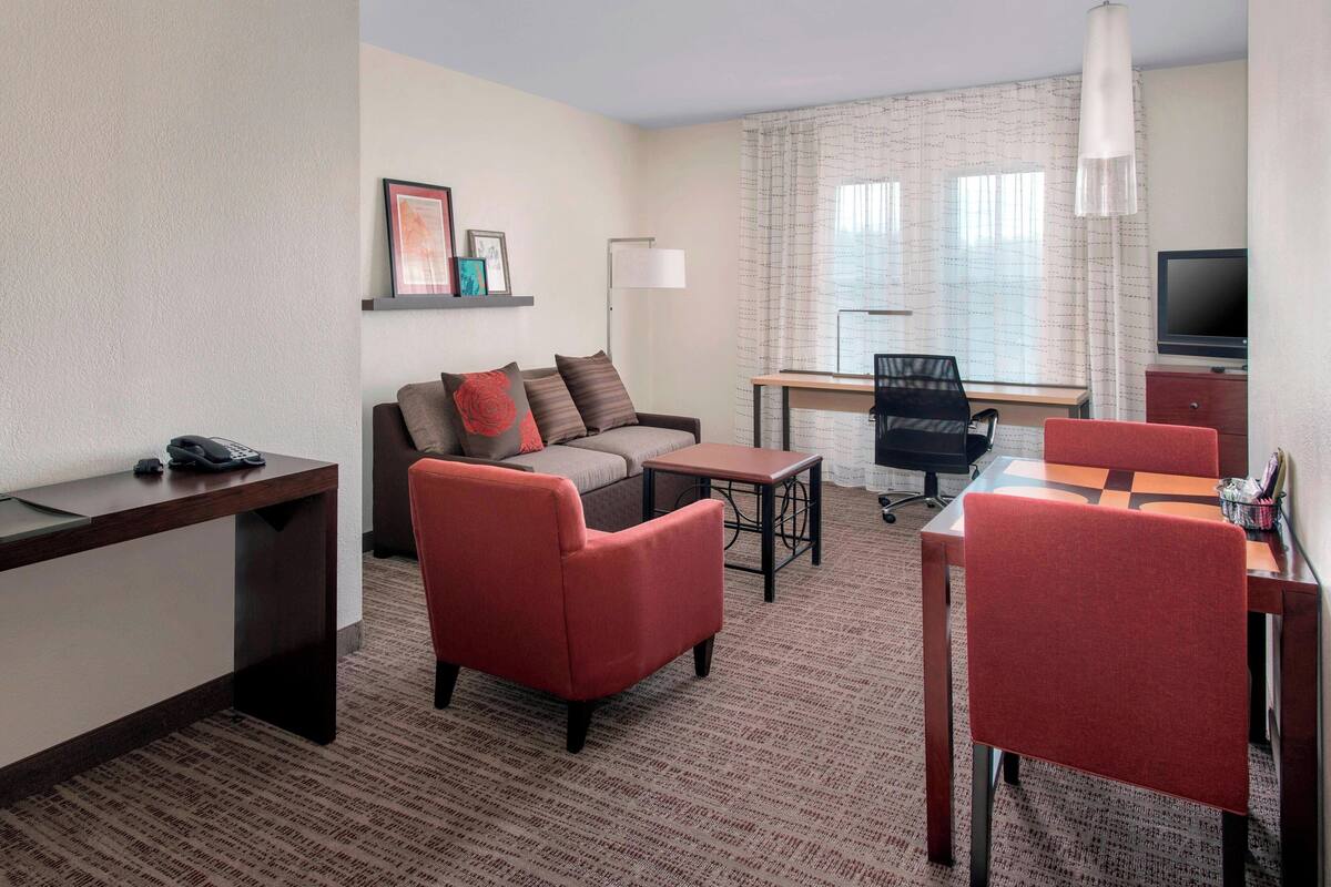 Una habitación de hotel con sofá, dos sillones, una mesita, un escritorio con teléfono, televisor y lámpara.