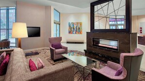 Una sala de estar moderna con un sofá, sillones, una mesa de centro, una chimenea, un televisor de pantalla plana y un ventanal grande.