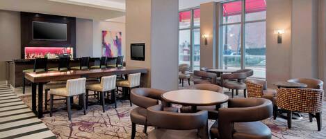 A hotel lobby with a bar area, seating arrangements, and large windows providing views.