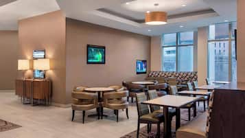 Un moderno vestíbulo de hotel con diversas opciones de asientos, incluyendo cabinas y mesas, y un ventanal con vistas a la ciudad.