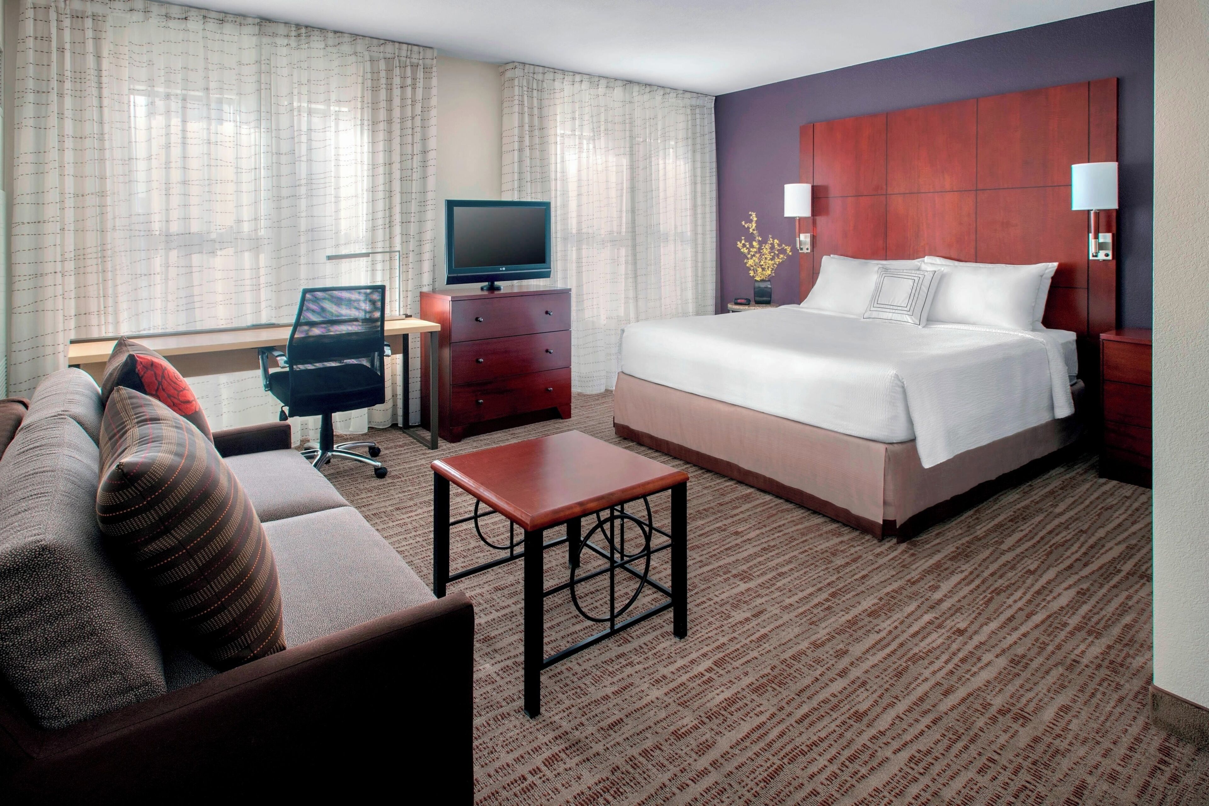 A hotel room with a bed, a desk, a chair, a television, and a small table.