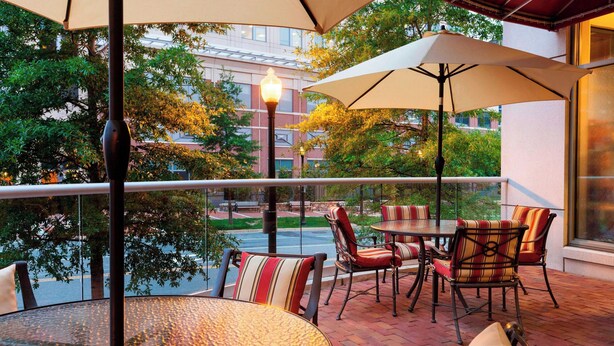 Un patio al aire libre con mesas y sillas redondas, sombrillas y vistas a un edificio y árboles.