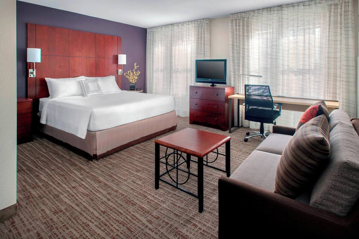 Una habitación de hotel con una cama grande, un escritorio con una silla, un televisor y un sofá con almohadas.