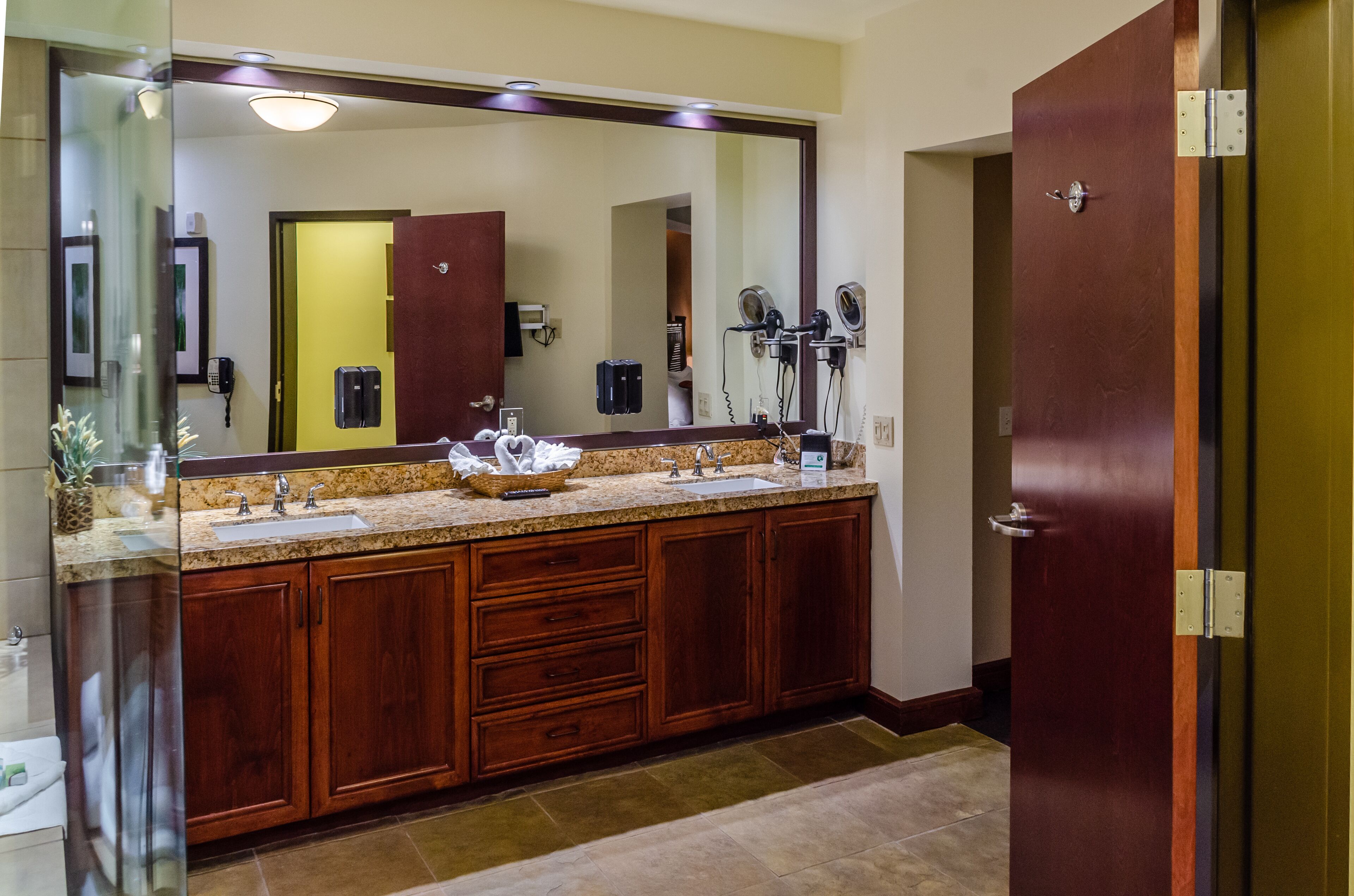 Une salle de bain d’hôtel avec un grand miroir, des meubles en bois, un comptoir en granit et un lavabo.