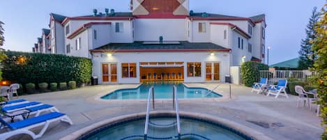 A hotel with a swimming pool, lounge chairs, and a covered patio area.