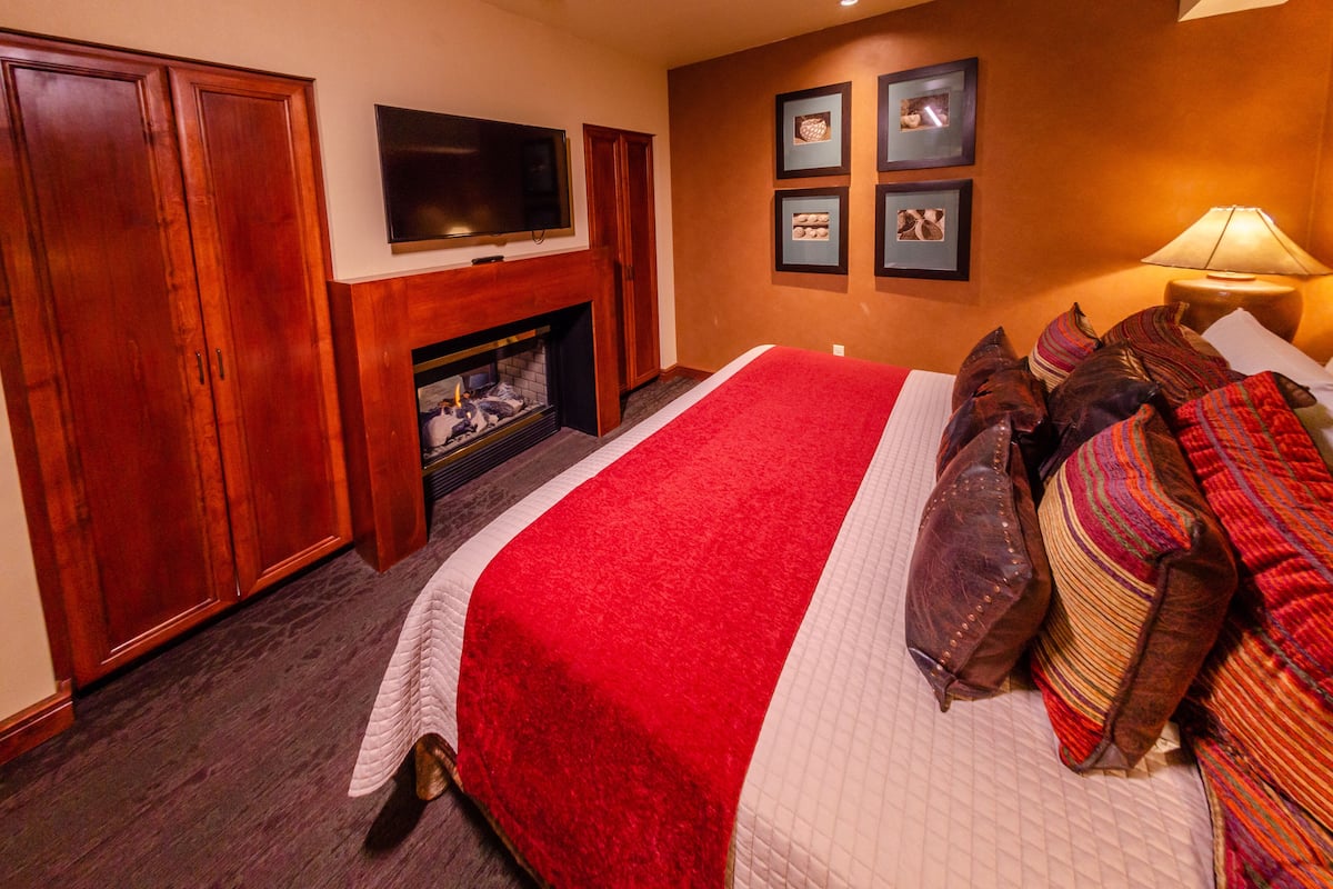 Habitación de hotel con una cama grande, chimenea, armario de madera y cuadros en la pared.