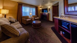 A hotel room with a sofa set, a round coffee table, a TV, a fireplace, and a minibar.