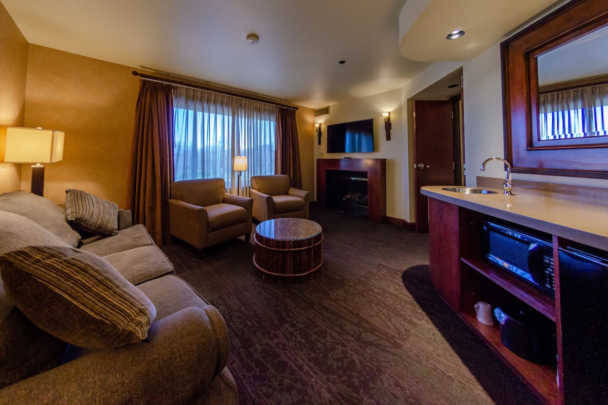 Habitación de hotel con sofá, una mesita redonda, televisor, chimenea y minibar.