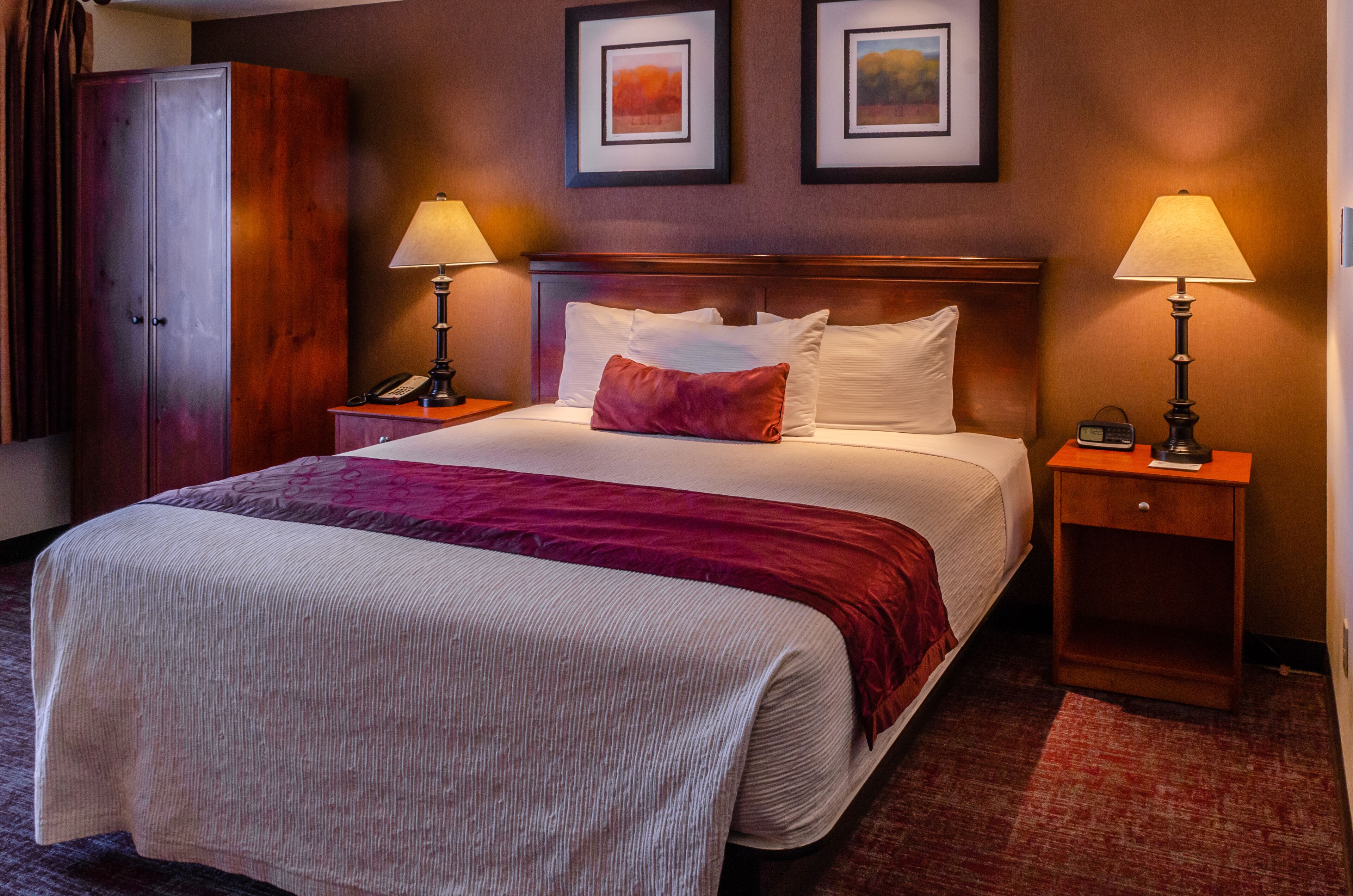 A hotel room with a large bed, two bedside tables, a wardrobe, and framed artwork on the wall.