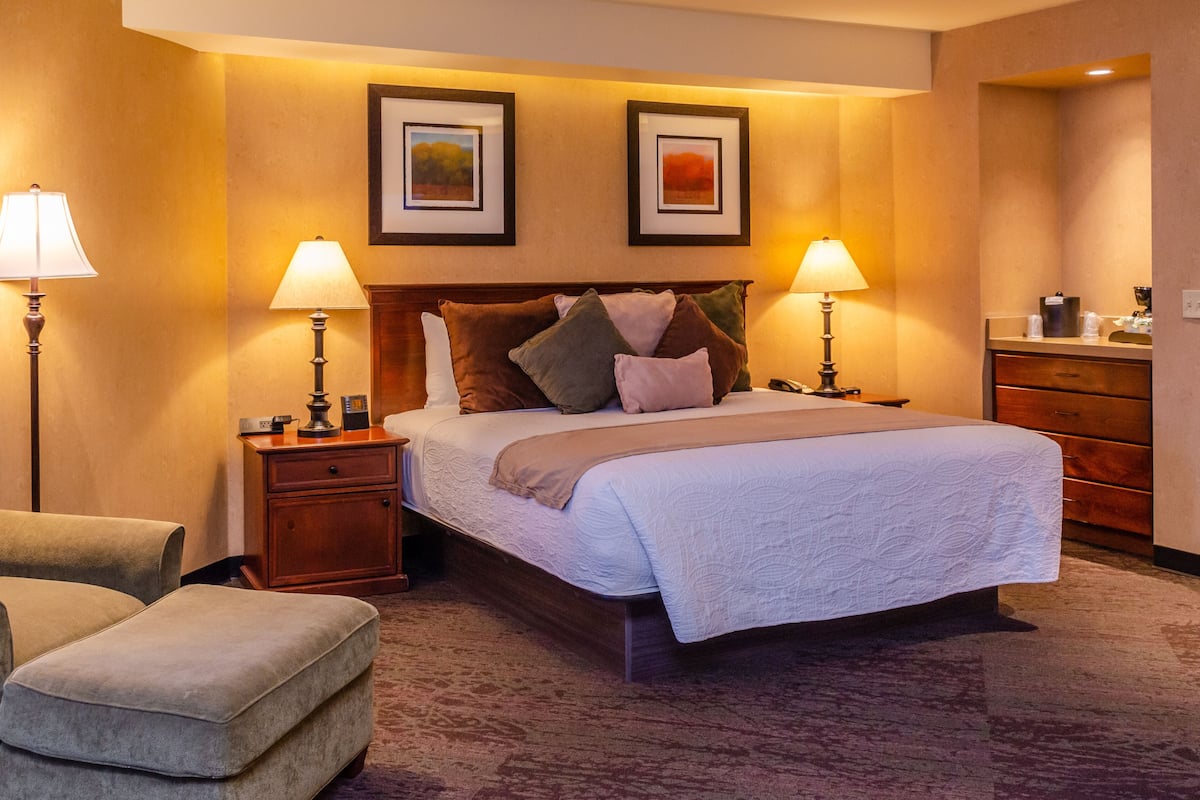 Una habitación de hotel con una cama grande, dos lámparas de noche, una mesita de noche de madera, un aparador de madera y dos cuadros enmarcados en la pared.