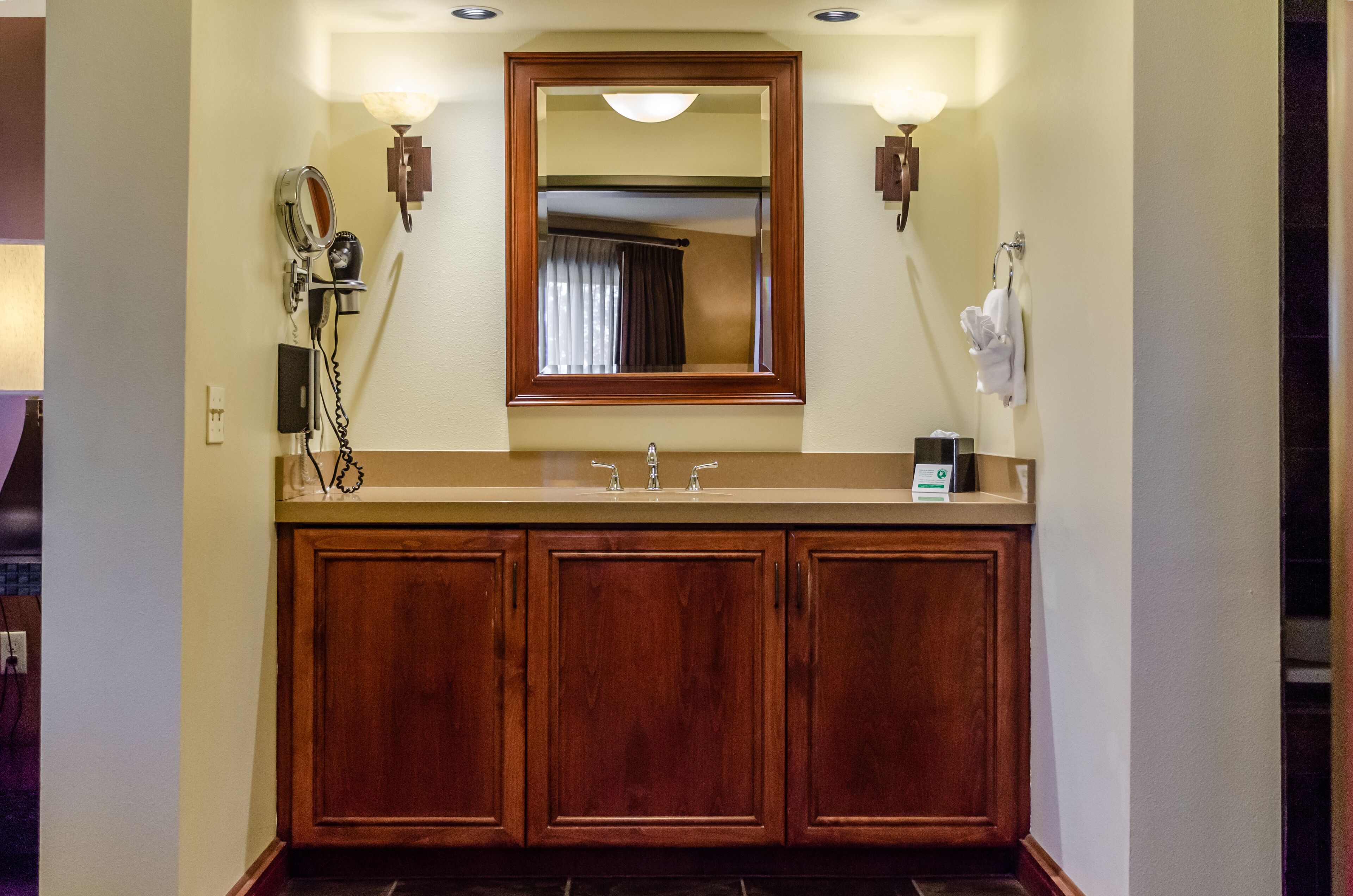A bathroom with a wooden vanity, a mirror, and two wall-mounted lights.