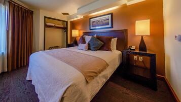 Habitación de hotel con una cama grande, una mesita de noche con lámpara, un armario y un cuadro en la pared.